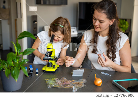 Mother and daughter examining various plant samples under a microscope at home. Concept of family science education and botanical exploration Mother and daughter examining various plant samples under a microscope at home. Concept of family science education and botanical exploration 127766900