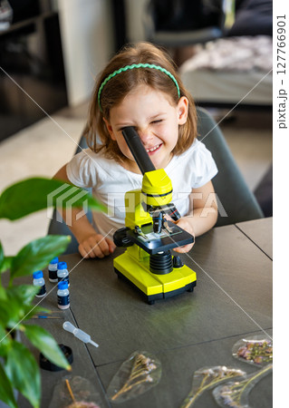 Little girl looking through a green microscope. Concept of curiosity and early scientific exploration 127766901