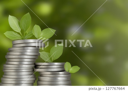 Stack of silver coins with green plants sprouting from them, glowing eco-friendly light 127767664