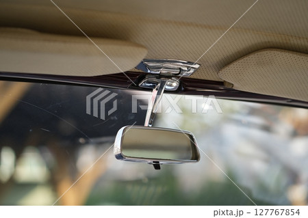 The rearview mirror of a classic car has a shiny chrome finish with a simple design, serving as a practical feature that adds elegance to the interior. 127767854