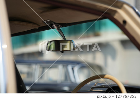 The rearview mirror of a classic car has a shiny chrome finish with a simple design, serving as a practical feature that adds elegance to the interior. 127767855