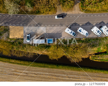 Aerial view of a forested landscape with camper vans parked along a roadside under a clear blue sky, with scenic woodland stretching toward the horizon. 127768009