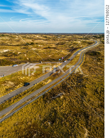 Aerial view of a coastal landscape with lush greenery, sandy dunes, and a winding road, showcasing the harmony of nature and infrastructure. Aerial view of a coastal landscape with lush greenery, sandy dunes, and a winding road, showcasing the harmony of nature and infrastructure. 127768012