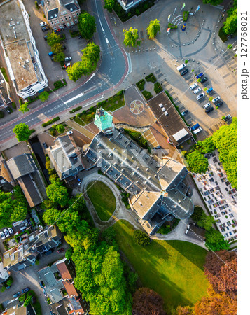 Aerial view of a picturesque European town featuring a prominent church with a tall green spire surrounded by lush greenery, quaint houses, and a town square with parked cars. Aerial view of a picturesque European town featuring a prominent church with a tall green spire surrounded by lush greenery, quaint houses, and a town square with parked cars. 127768021