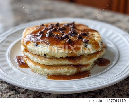 Pancake stack with chocolate chunks and caramel topping. Sweet rustic breakfast in cozy home setting. 127769110