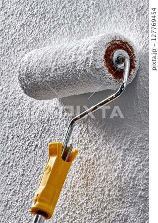 White paint roller on wall with fresh coat of paint and bright yellow handle 127769454