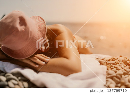A woman sunbathes on the beach, lying on her stomach in a red swimsuit against the sea backdrop. A woman sunbathes on the beach, lying on her stomach in a red swimsuit against the sea backdrop. 127769710