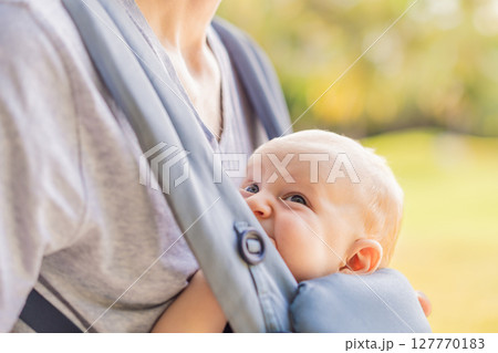 Young father walks in nature with his baby son nestled close in a parent-facing ergonomic baby carrier. Bonding, warmth, and modern parenting concept in a peaceful outdoor setting 127770183