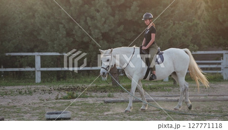 Horseback riding training, young jockey riding white horse in the paddock during golden hour sunset, equestrian sport, active lifestyle, love and care for animals 127771118