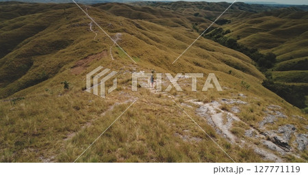 Woman walking on a path in the middle of rolling hills covered with dry grass in Sumba Island, Indonesia, enjoying the landscape during a sunny summer day Woman walking on a path in the middle of rolling hills covered with dry grass in Sumba Island, Indonesia, enjoying the landscape during a sunny summer day 127771119