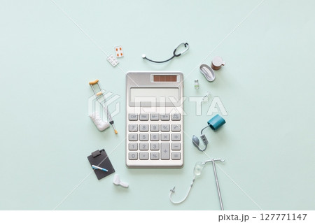 電卓とミニチュアの聴診器、血圧計、松葉杖、薬、点滴、注射器などの医療用品　医療費や保険のイメージ 127771147