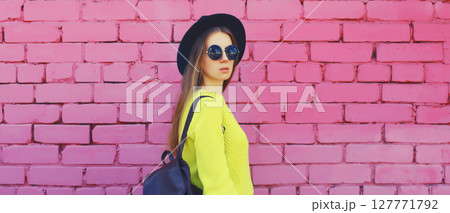 Stylish young woman in black hat, yellow sweater with backpack, girl posing on urban wall background 127771792