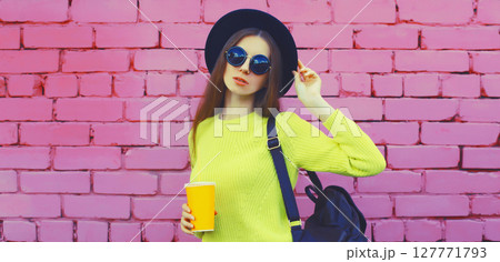 Stylish young woman in black hat, yellow sweater with backpack, girl posing on urban wall background 127771793