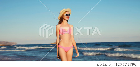 Summer vacation, beautiful happy slim woman in pink bikini swimsuit, tourist hat on the beach on sea 127771796