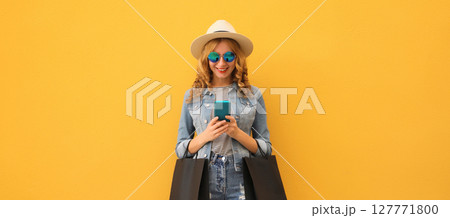 Beautiful happy young woman holding phone with black shopping bag, summer hat on yellow background Beautiful happy young woman holding phone with black shopping bag, summer hat on yellow background 127771800