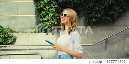 Stylish modern happy smiling young woman with phone in city park, girl holding smartphone on street 127771801