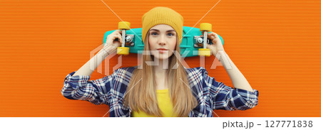 Portrait of stylish young girl with skateboard in hat, modern teenage female posing on orange 127771838