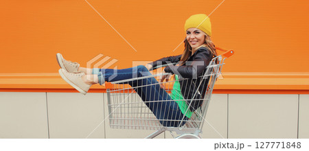 Beautiful happy smiling young blonde woman having fun sitting in shopping trolley cart in the city Beautiful happy smiling young blonde woman having fun sitting in shopping trolley cart in the city 127771848