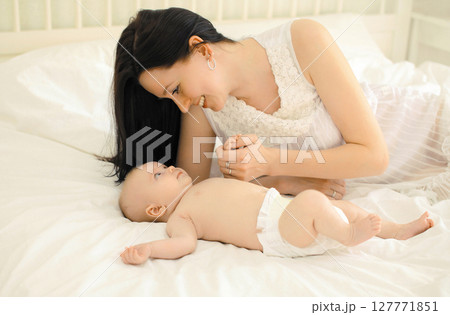Happy young mother playing with cute baby lying together on the bed at home Happy young mother playing with cute baby lying together on the bed at home 127771851
