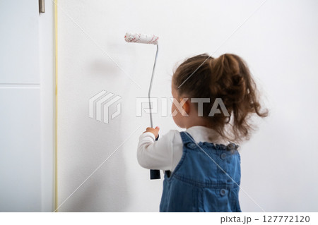 Creative little girl decorating the apartment painting a wall in casual clothes.  127772120