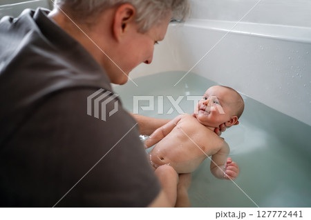 Top view smiling baby bathing and swimming in the bath. Baby learning to swim and playing sports. Father enjoys bath time with his curious baby in a cozy bathroom. Fatherhood concept. Selective focus. Top view smiling baby bathing and swimming in the bath. Baby learning to swim and playing sports. Father enjoys bath time with his curious baby in a cozy bathroom. Fatherhood concept. Selective focus. 127772441