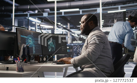 Exhausted server farm employee stretching back after sitting too long at computer desk. Fatigued man in data center office relaxing muscles, stressed by long hardware troubleshooting session, camera A 127772537