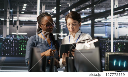 Data center teamworking colleagues performing maintenance on server racks used for artificial intelligence processing. Engineering team managing server hub rigs used for machine learning, camera A 127772539