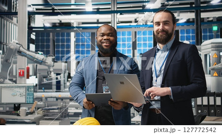 Team of diverse analysts consultants reviewing data and checklists in a high tech solar panel plant, ensuring manufacturing process meets sustainable energy and innovation standards. Camera A. Team of diverse analysts consultants reviewing data and checklists in a high tech solar panel plant, ensuring manufacturing process meets sustainable energy and innovation standards. Camera A. 127772542