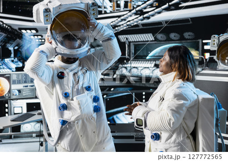 Researcher travelling in space with starship putting helmet on, talking with colleague, conducting scientific experiments. Scientist dressing in equipment, chatting with coworker during cosmic journey Researcher travelling in space with starship putting helmet on, talking with colleague, conducting scientific experiments. Scientist dressing in equipment, chatting with coworker during cosmic journey 127772565