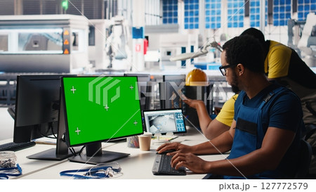 African american male engineer does troubleshooting on copy space display, fixing errors to ensure seamless solar panels manufacturing. Technician works in the assembly line. Camera B. 127772579
