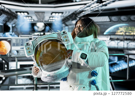 Astronaut holds helmet inside space station, preparing for mission outside, on hostile planetary habitat. Starship crew member beginning landing procedures on extraterrestrial planet Astronaut holds helmet inside space station, preparing for mission outside, on hostile planetary habitat. Starship crew member beginning landing procedures on extraterrestrial planet 127772580