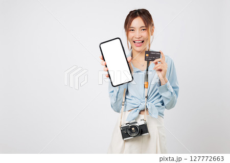 Travel phone and travel app shown by smiling Happy tourist young woman. She holds credit card bank, photo camera, and displays blank screen during fun trip. tourism isolated studio white background 127772663