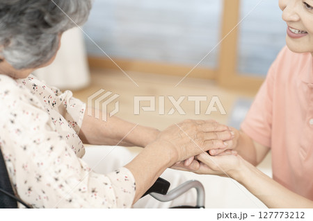 車椅子のシニア女性と話をする女性介護士　ボディパーツ　握手　手を握る　コミニュケーション 127773212