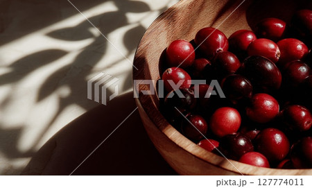 Red Cranberries in Wooden Bowl with Sunlight and Leaf Shadows 127774011