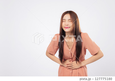 Stomach pain and stomach pressure visibly affect an Asian woman with eyes closed holding her abdomen from cramp or health issue isolated on studio white background Stomach pain and stomach pressure visibly affect an Asian woman with eyes closed holding her abdomen from cramp or health issue isolated on studio white background 127775180