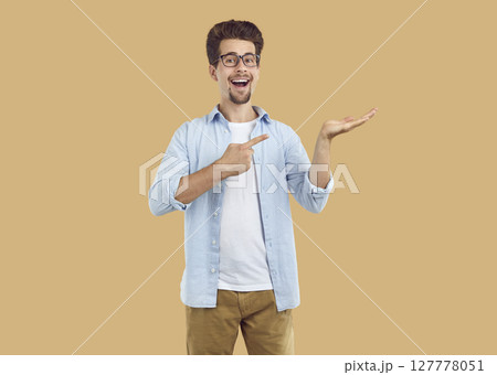 Laughing happy bearded man pointing index fingerand hand on copy space on beige background. 127778051