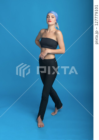 Portrait of beautiful woman with tight dark sport clothing standing in blue studio background Portrait of beautiful woman with tight dark sport clothing standing in blue studio background 127779101