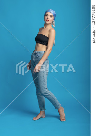 Portrait of beautiful woman with tight black bra and jeans standing in blue studio background 127779109