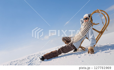 Child is resting on a sleigh in the snow. 127781969