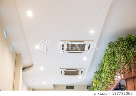Modern white ceiling with cassette type air conditioner for cool comfort. indoor ventilation system provides clean air and climate control alongside recessed spotlights 127782069