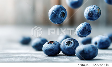 Fresh blueberries are falling onto a textured surface, showcasing their vibrant color and natural beauty in a dynamic and appetizing arrangement 127784510