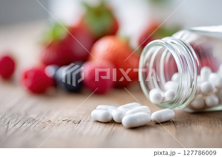 White Pills Spilled From Glass Jar with Fresh Berries in Background 127786009