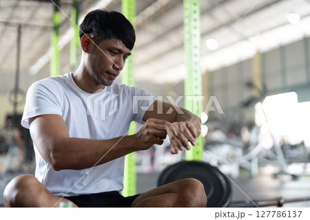 Fitness and Focus. Young man adjusting smartwatch while exercising in gym. 127786137