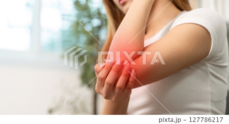 Elbow Pain Awareness. Woman holding her elbow in discomfort at home. 127786217