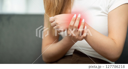 Wrist Pain Relief. Young woman holding wrist in discomfort, seeking relief from pain. 127786218