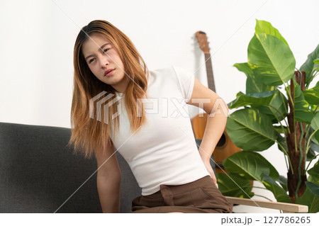 Back Pain Awareness. Young woman sitting with discomfort, holding her lower back. Back Pain Awareness. Young woman sitting with discomfort, holding her lower back. 127786265