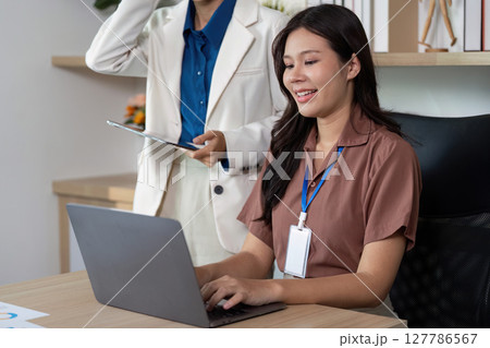 Productivity in the Office. Woman smiling while working on a laptop with a supportive colleague. 127786567