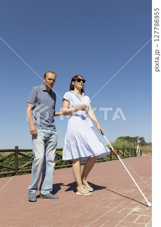 Man guiding blind woman with white cane on sunny day Man guiding blind woman with white cane on sunny day 127786955