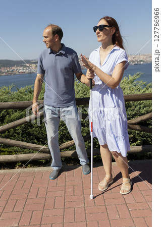 Blind woman holding white cane talking with man outdoors 127786966
