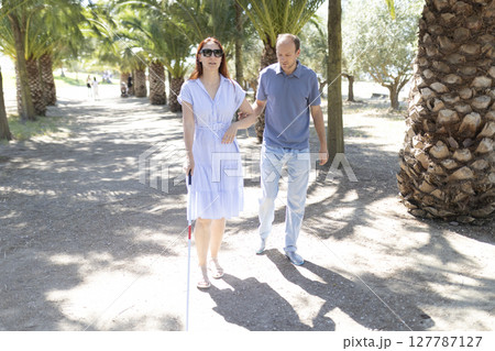 Man helping blind woman walking in a palm tree park 127787127